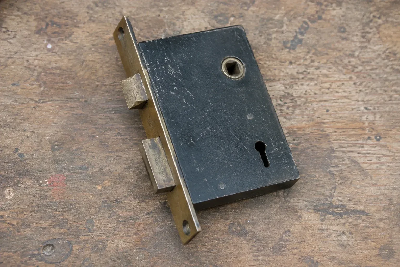Closed mortise lock case with spindle opening, keyhole, latch and deadbolt on a wooden workbench. — Vintage Mortise Lock Service, Richmond Hill